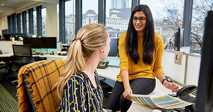 Two colleagues discussing work at their desk