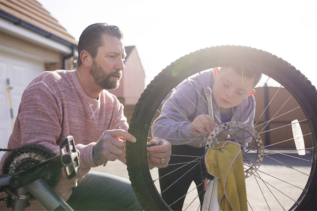 A male carer servicing a bicycle with a young boy