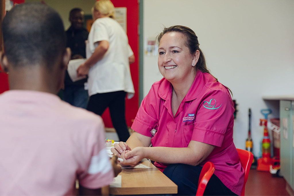 Female clinician in pink tunic speaking to a patient